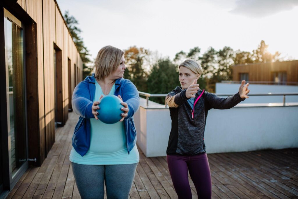 A woman engaging in a guided fitness session with a personal trainer, focusing on movement and strength training. This represents Raleigh Weight Loss Center's holistic approach to weight loss, which includes personalized coaching, metabolic reset, and sustainable lifestyle changes.